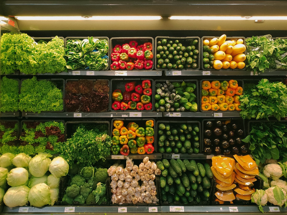 A grocery store aisle with fresh produce and a shopping cart full of healthy vegetables