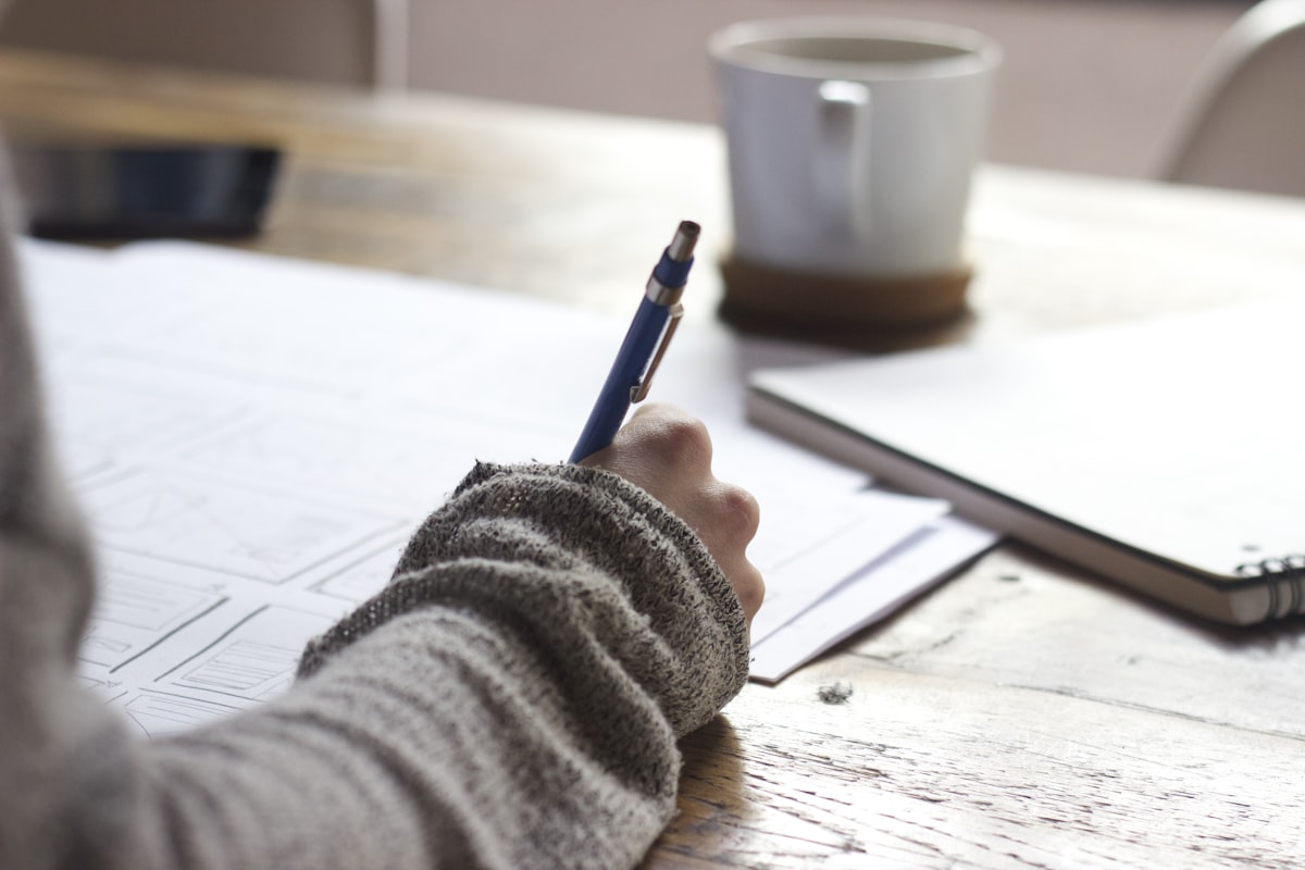 A person taking notes and completing an online research survey on a laptop with coffee