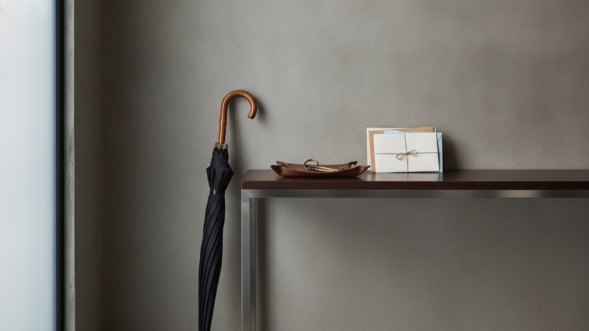 A closed umbrella resting by an entryway table with house keys in natural light